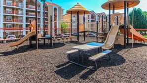 Un parque infantil con toboganes y mesas, rodeado de edificios de varios pisos con balcones.