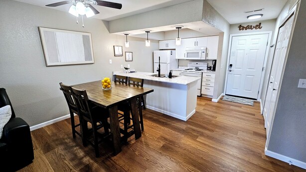 Una cocina moderna con armarios blancos, una isla central y un comedor con mesa y sillas de madera.