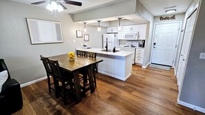 A modern kitchen with white cabinets, a central island, and a dining area with a wooden table and chairs. - Remodeled 2BR Condo • 2 Min to Branson Strip • Sleeps 6 • 2 Pools/Slide/Hot Tub! (Branson)