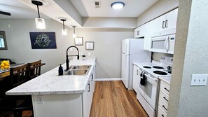 A modern kitchen with white appliances, a marble countertop, and pendant lighting. - Remodeled 2BR Condo • 2 Min to Branson Strip • Sleeps 6 • 2 Pools/Slide/Hot Tub! (Branson)