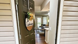 Una puerta con un felpudo que dice 'hello', un letrero que dice 'cubbhouse' y vista a una zona de cocina.