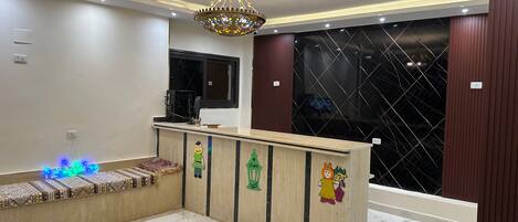 A reception area with a marble floor, a decorative chandelier, a wooden reception desk with cartoon character decorations, and a large window with a black mesh screen.