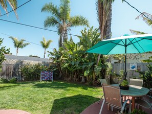 Un jardin avec une table et des chaises de patio, entouré d’une végétation luxuriante et d’une clôture en bois.