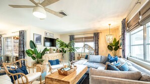 Un salon avec un ventilateur de plafond, une table basse, un canapé et un téléviseur fixé au mur.