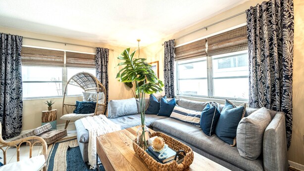 Un salon chaleureux avec un canapé, une table basse et un fauteuil. On trouve une plante sur la table basse et une fenêtre avec des rideaux.