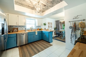 A modern kitchen with blue cabinets, stainless steel appliances, a wooden ceiling, and a hanging pot rack.