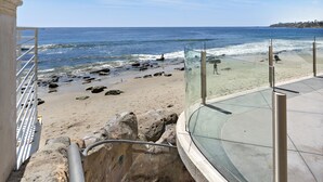 A beach view from a balcony with a glass railing, a staircase leading down to the beach, and a sandy shore with rocks. - 3 Unobstructed ocean view direct beach access! Oceanfront Villa with a Spectacular View (C) (Laguna Beach)