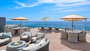 An outdoor patio with wicker furniture, a fire pit, and umbrellas overlooking the ocean. - 3 Unobstructed ocean view direct beach access! Oceanfront Villa with a Spectacular View (C) (Laguna Beach)