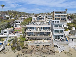 Une propriété côtière à plusieurs étages, dotée d’un grand balcon, d’un espace salon extérieur et d’un rivage rocheux.