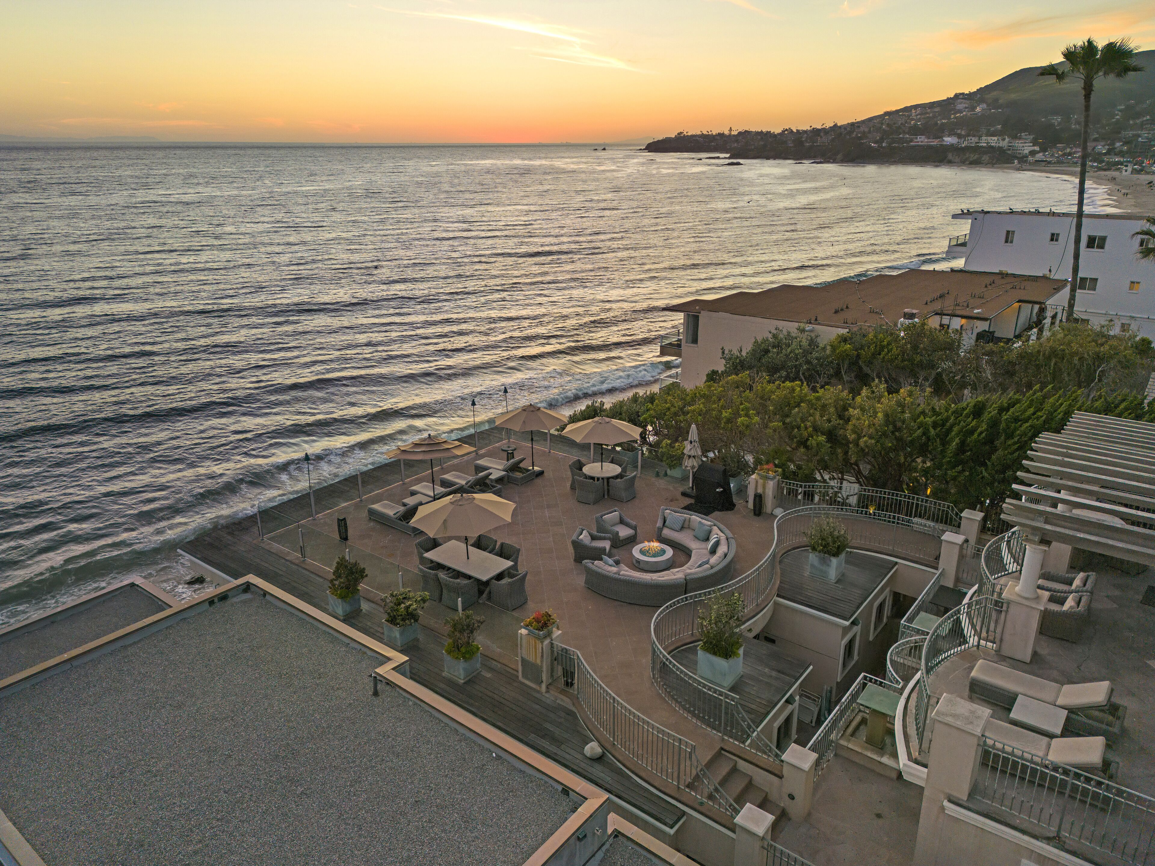 Una terraza en la azotea con mobiliario exterior, un brasero y vista al océano al atardecer.