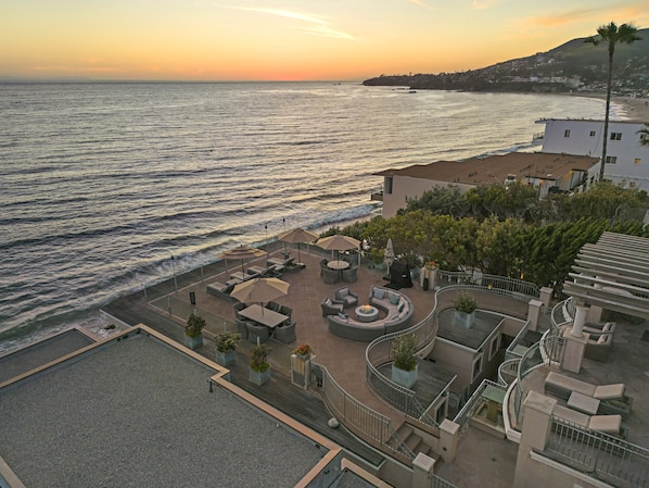 Une terrasse sur le toit avec des sièges extérieurs, un foyer et une vue sur l’océan au coucher du soleil.