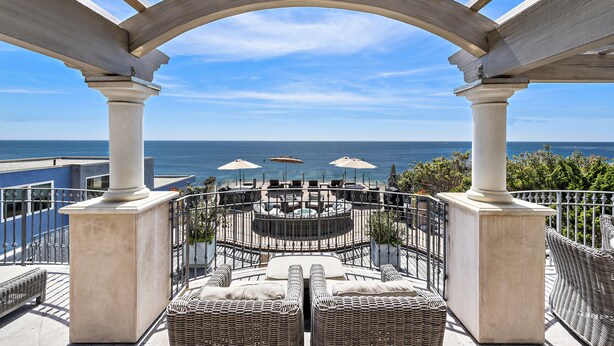 Une terrasse avec des sièges extérieurs, un foyer circulaire et une vue sur l’océan.