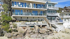 Une propriété moderne située en bord de mer, dotée de plusieurs balcons, d’une piscine et entourée d’un paysage rocheux.