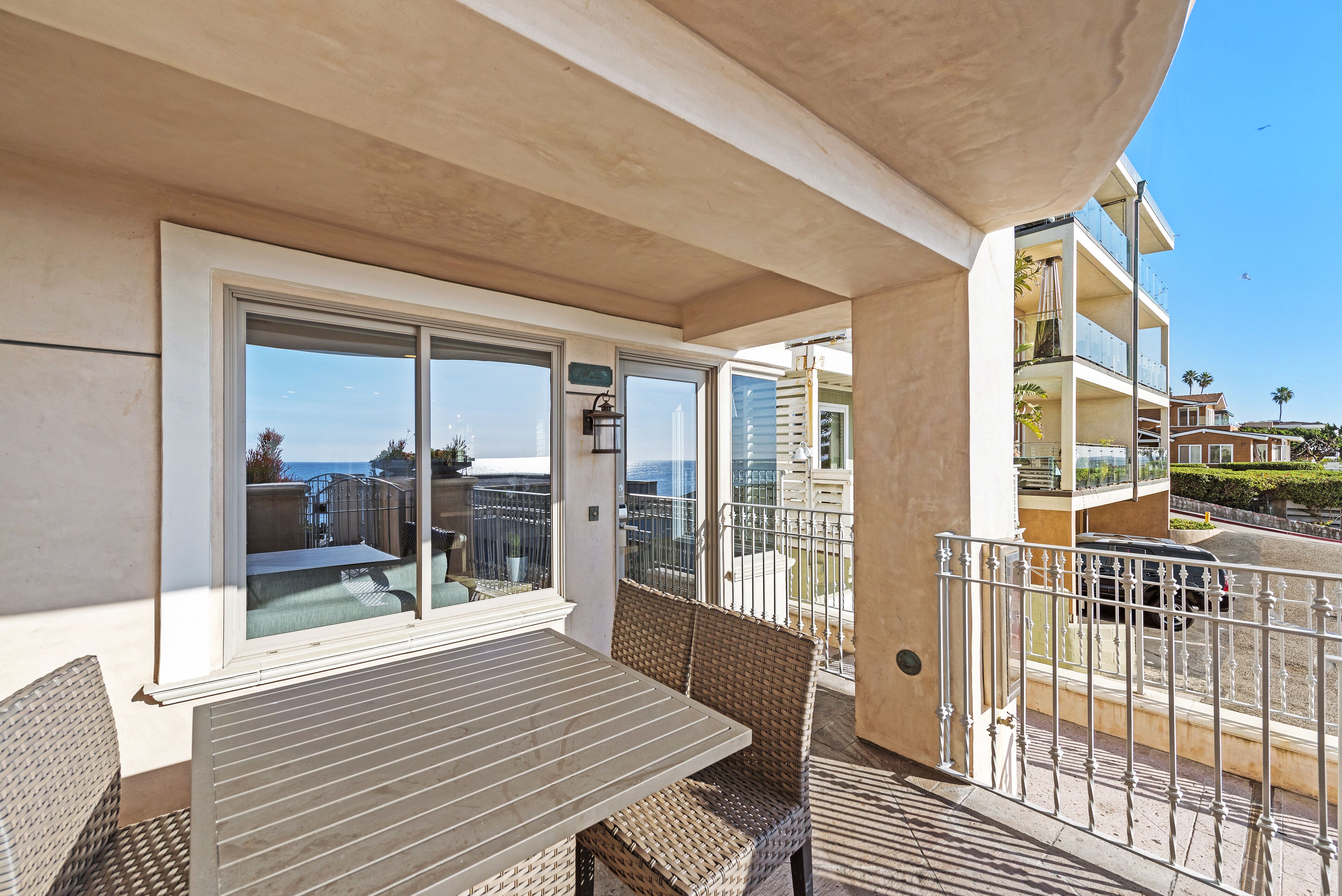 A balcony with a table and chairs, a view of the sea, and a building with balconies.