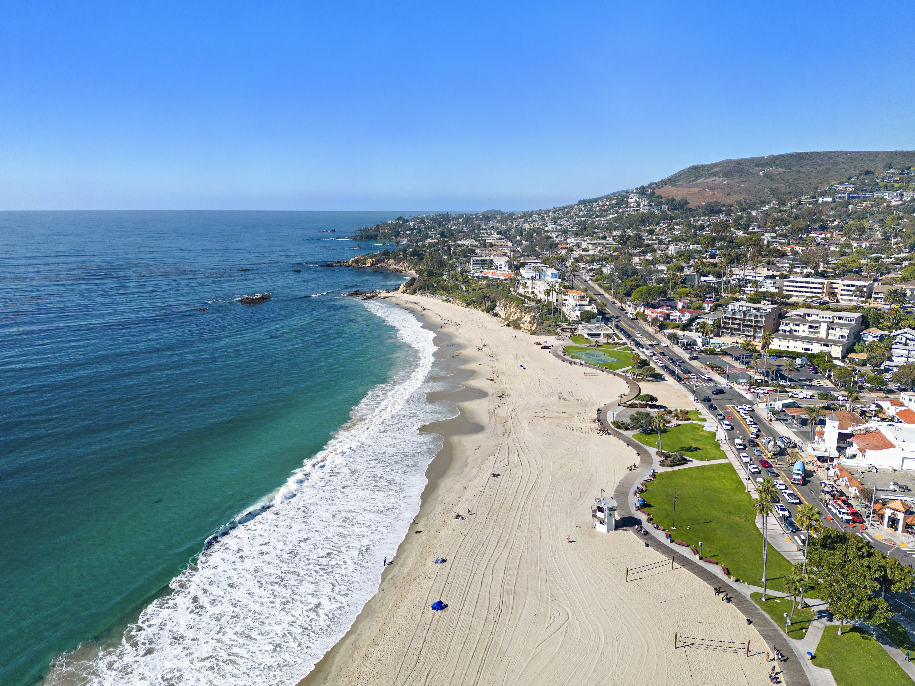 A coastal town with a beach, residential buildings, and a hilly backdrop.