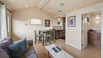 A spacious living area with a sofa, a dining table with chairs, a kitchen in the background, and a hallway leading to a bedroom.