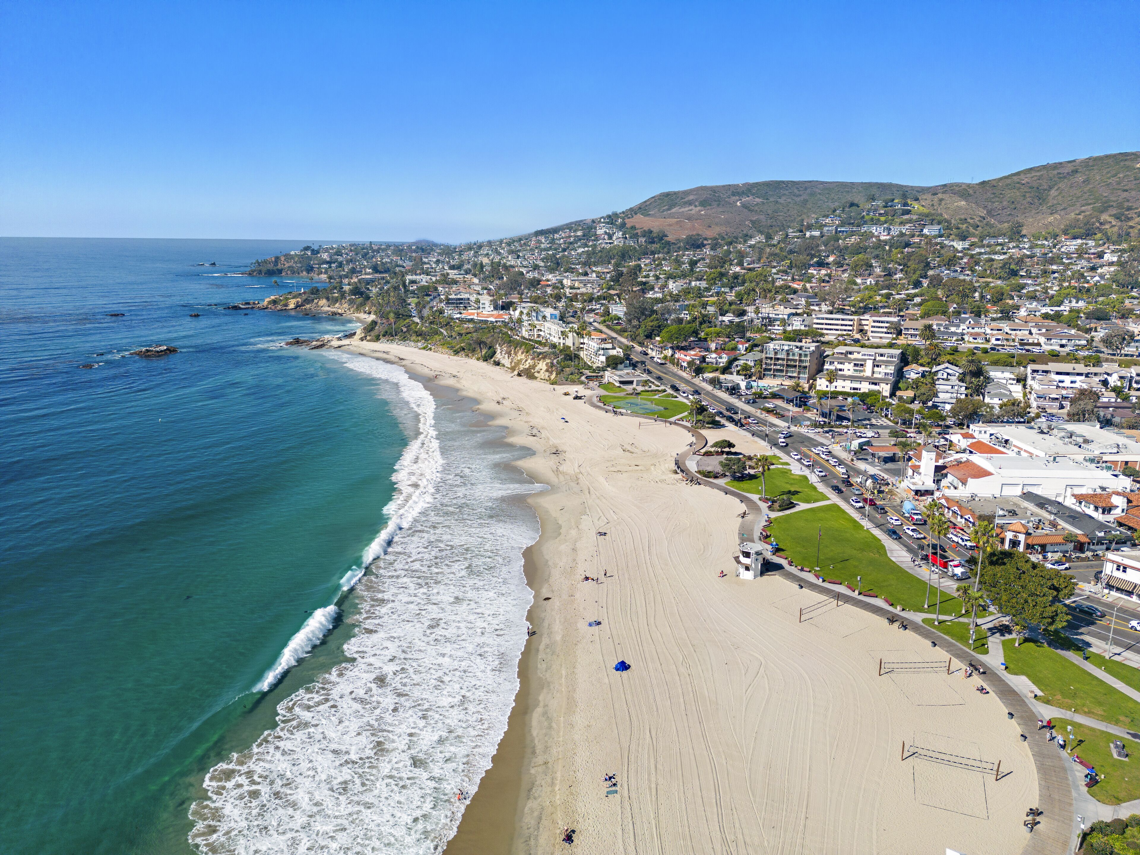 A coastal town with a beach, residential buildings, and a hilly backdrop.