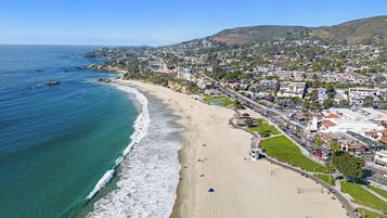 A coastal town with a beach, residential buildings, and a hilly backdrop.