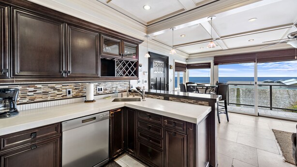 A modern kitchen with dark cabinetry, a large island, and a view to a balcony with a glass door. - Ocean View Villa, walk to main beach, easy beach access (Laguna Beach)