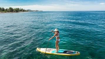 Eine Person steht auf einem Paddleboard auf ruhigem, blauem Meer, im Hintergrund eine Küstenlinie.