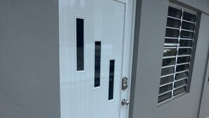 Una puerta blanca con dos ventanas rectangulares y un picaporte metálico, junto a una ventana con persianas horizontales.