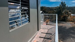 Un edificio con una ventana que refleja nubes y palmeras, un balcón con barandilla y vistas a un paisaje montañoso.