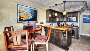 A kitchen with dark wood cabinets, a central island, stainless steel appliances, pendant lighting, and a large framed picture on the wall. - Breathtaking Views Savor the Sunset, Relax (Laguna Beach)