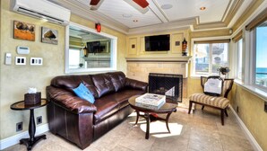 A living room with a leather sofa, a glass coffee table, a fireplace, and a ceiling fan. - Breathtaking Views Savor the Sunset, Relax (Laguna Beach)
