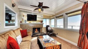 A living room with a fireplace, a sofa, a coffee table, a TV, and a ceiling fan. - Ocean views steps to the water prime Laguna Beach 8 Villa Roma (Laguna Beach)