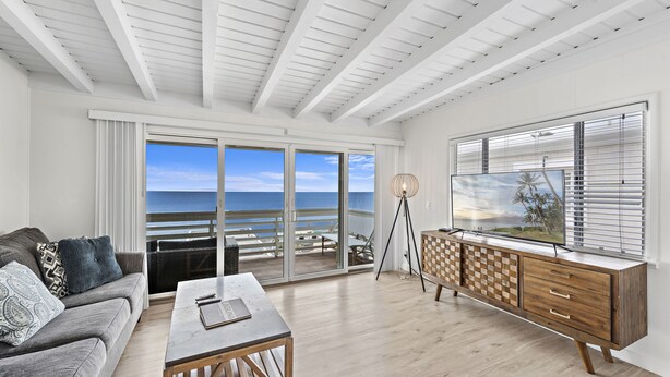 A modern living room with a large sliding glass door leading to a balcony with a view of the ocean.