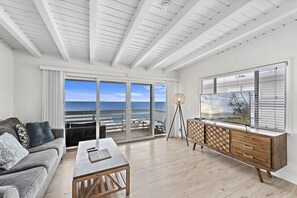 A modern living room with a large sliding glass door leading to a balcony with a view of the ocean.