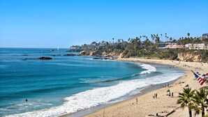 A beach with clear blue water, sandy shore, and palm trees.