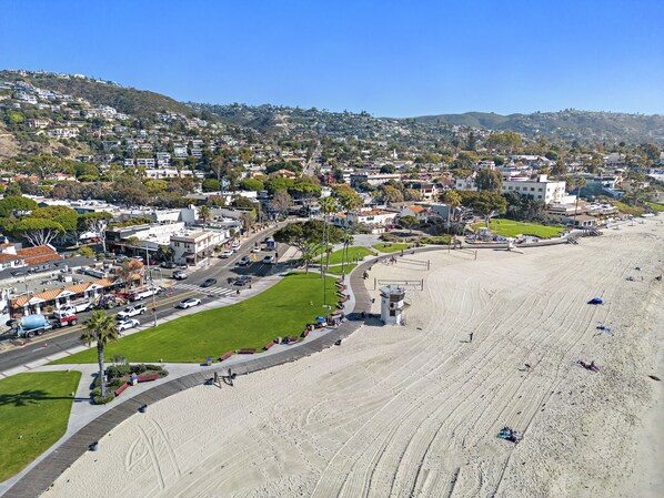 A coastal town with a wide sandy beach, residential areas, and a clear blue sky.