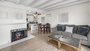 A modern living room with a fireplace, a dining area, and a kitchen in the background.