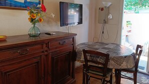 Une pièce avec un bureau en bois, un téléviseur fixé au mur, un vase rempli de fleurs et une nappe à motifs.