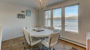 Une salle de conférence avec une table blanche, des fauteuils en cuir et un lustre. De grandes fenêtres offrent une vue sur un lac et des montagnes.
