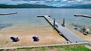Une jetée au bord du lac, avec une plage de sable et deux chaises bleues.