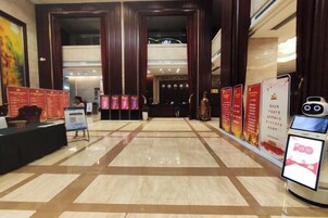 Un vestíbulo de hotel con mostrador de recepción, quiosco de información digital y varios carteles informativos rojos.
