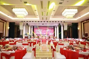 Un salón de banquetes con mesas redondas dispuestas en filas, un escenario con fondo y una araña.