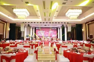 Un salón de banquetes con mesas redondas dispuestas en filas, un escenario con fondo y una araña.