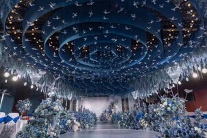 Un espacio con escenario circular, decoraciones colgantes y arreglos florales.