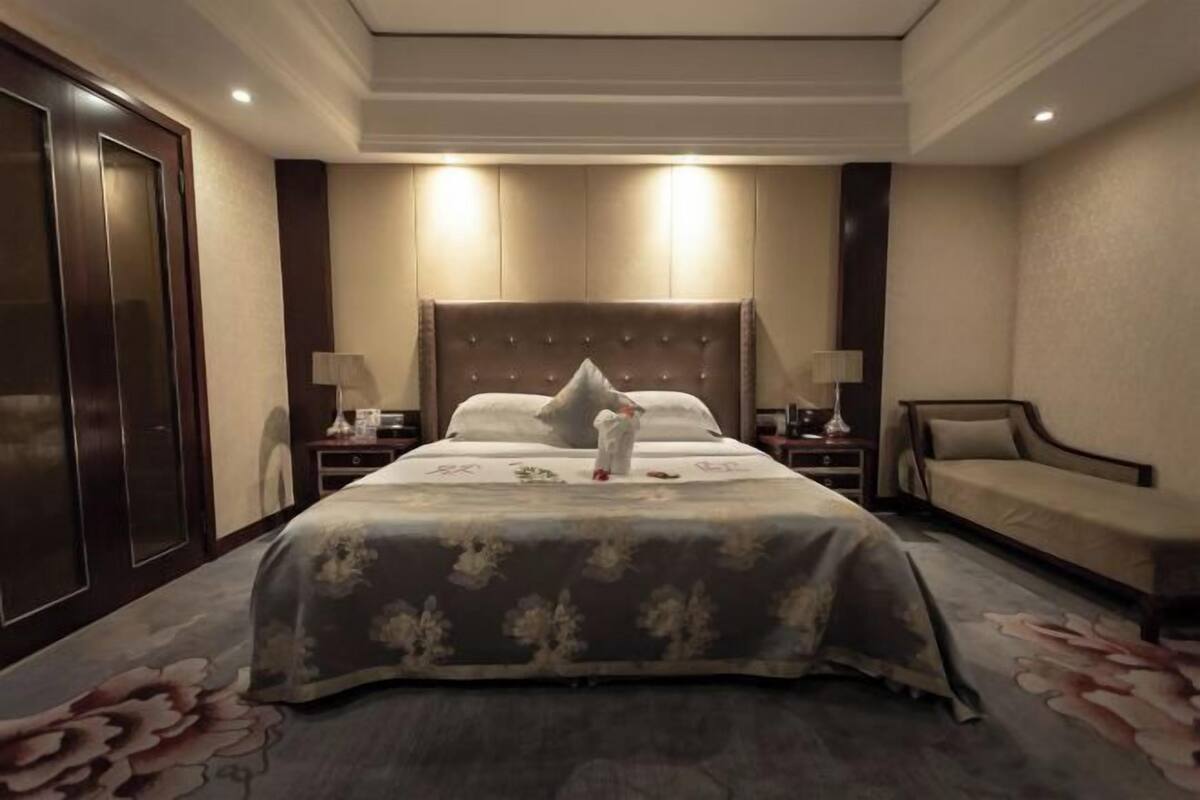 A hotel room with a large bed, two bedside tables, a nightstand, a sofa, and a door.