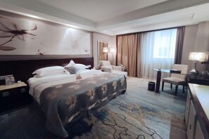 Una habitación de hotel con una cama grande, un escritorio, una silla y una ventana con cortinas.
