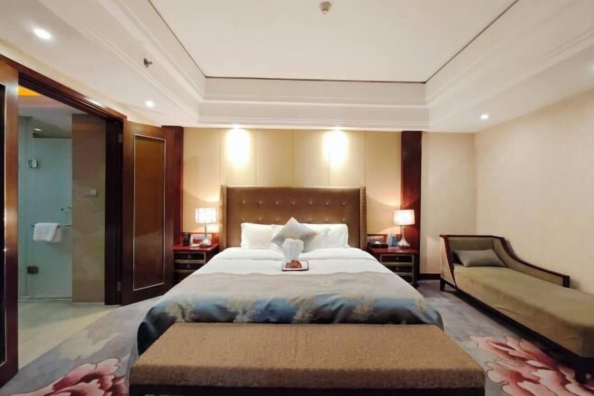 A hotel room with a large bed, bedside tables, a bench, and a sofa.