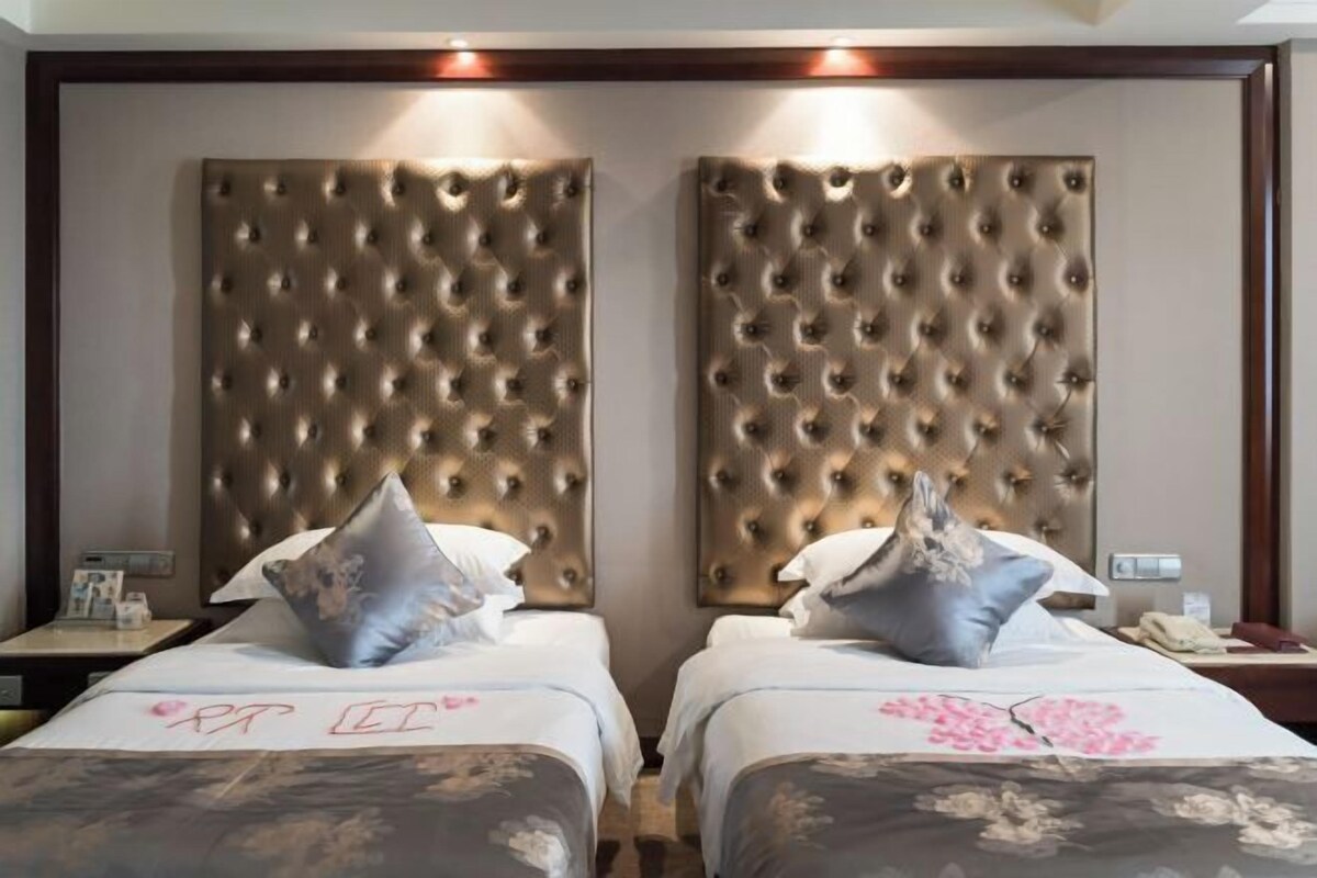Habitación de hotel con dos camas, cada una con cabecero capitonado, y una mesita de noche con lámpara y teléfono.