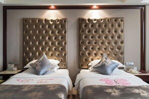 Habitación de hotel con dos camas, cada una con cabecero capitonado, y una mesita de noche con lámpara y teléfono.