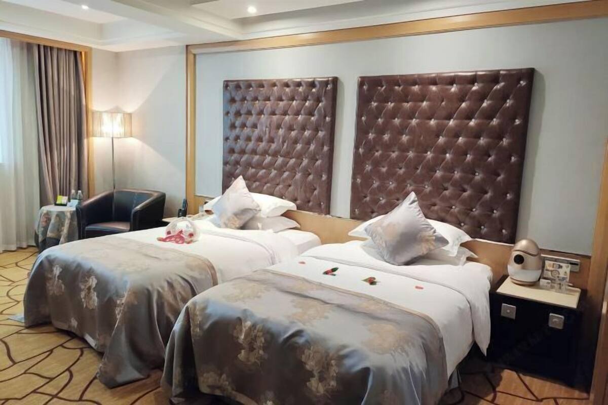 A hotel room with two beds, a nightstand with a lamp, and a chair.