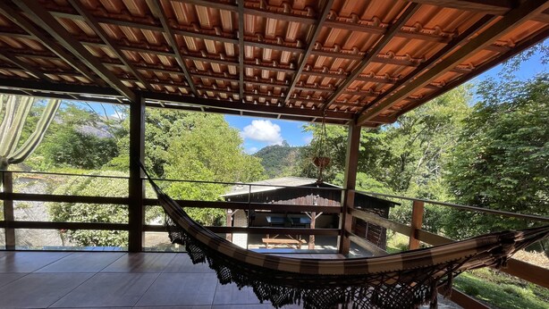 Un hamac sous un toit en bois, une terrasse en bois et une vue sur un bâtiment et des arbres.