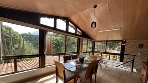 Un vaste espace dédié à la salle à manger, avec une table et des chaises en bois, de grandes fenêtres offrant une vue sur le paysage environnant et un plafond en bois.