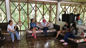 A group of people sitting on wicker sofas in a covered area with a wooden floor and a view of greenery through a lattice window. - Reserva Natural Yavary Tucano (Leticia)
